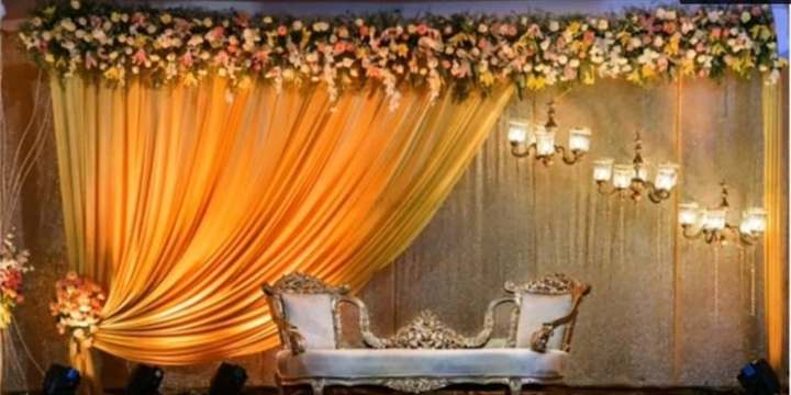 Reception stage with amber silk drape, floral canopy and hanging chandeliers