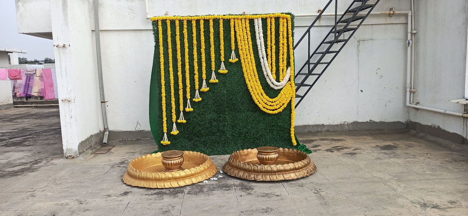 Green wall haldi backdrop with marigold strings and brass urlis