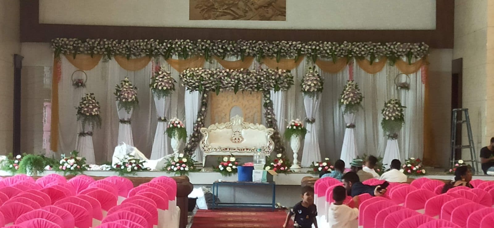 Hall wedding stage with floral arch facing pink guest chairs